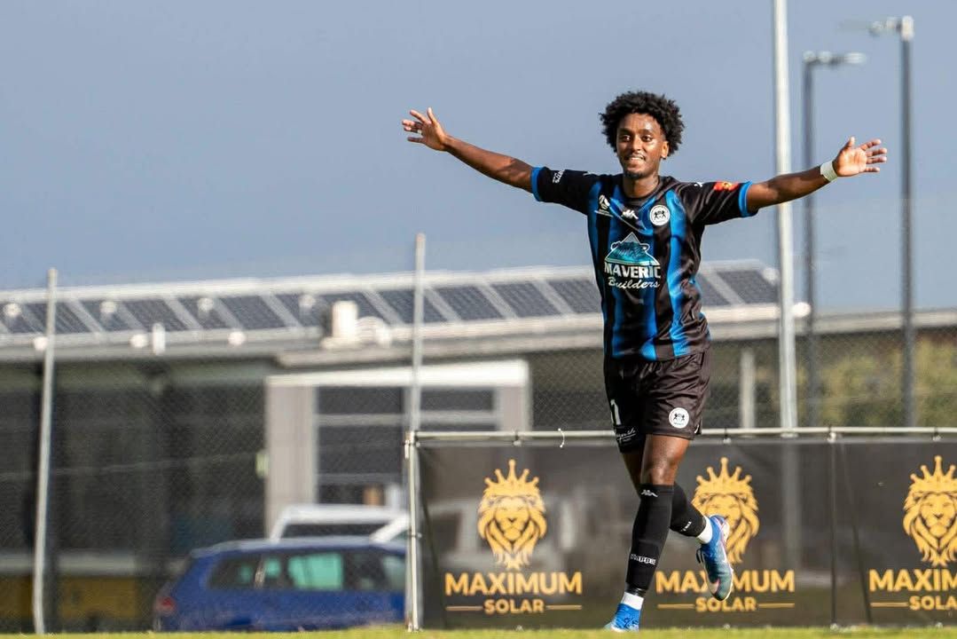 A soccer player celebrating with arms outstretched in front of Maximum Solar signage
