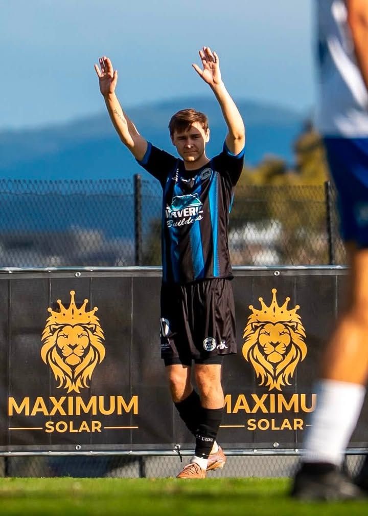 A soccer player raising both arms in front of Maximum Solar banners
